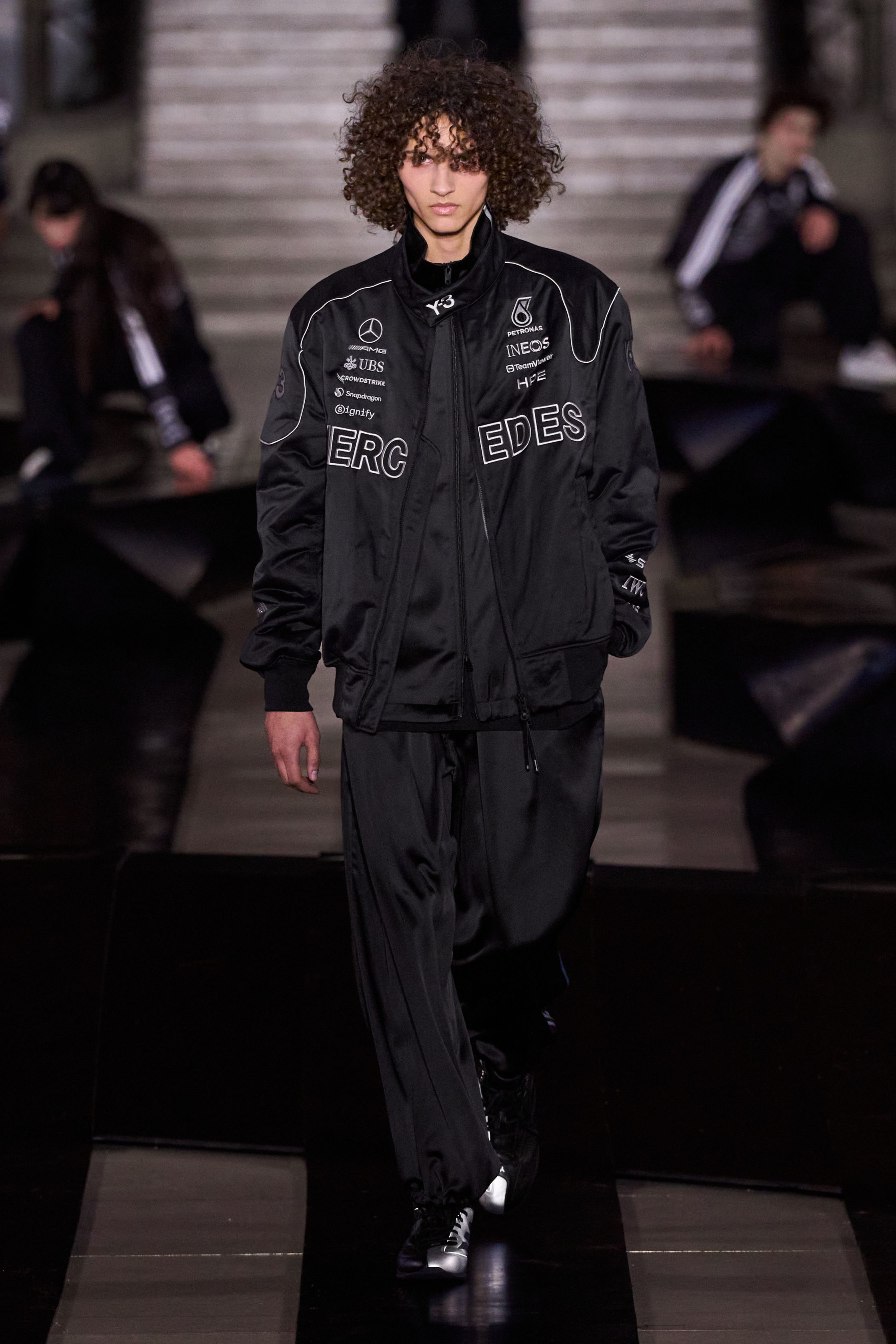Y-3 2026 秋冬回到品牌最具力量感的“机能—反叛”核心。红黑主调贯穿全场，军装式羽绒、飞行员夹克与运动裤在宽阔比例中形成高度压迫的队列感。模特如同匿名个体行走于冷峻场景中，服装成为对秩序、权威与都市焦虑的视觉回应。本季弱化潮流化装饰，强化制服感与防护属性，体现 Yohji Yamamoto 的哲学克制与 adidas 的功能理性在极端现实语境下的再次融合-顽石频道趋势研究